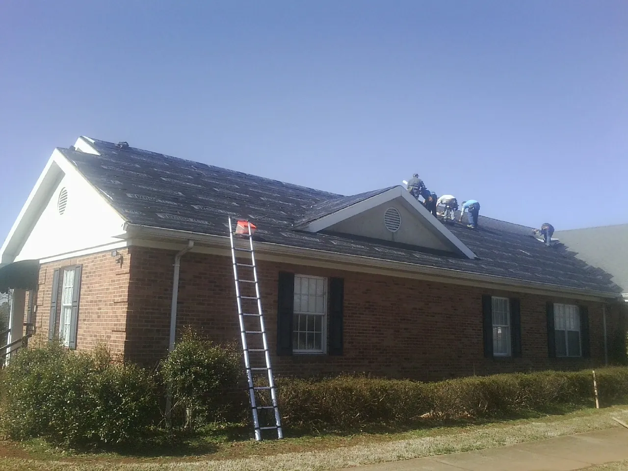 Crew tearing shingles off a brick ranch roof with a ladder set — Metal Roof Repair work by our crew in Taylors Falls