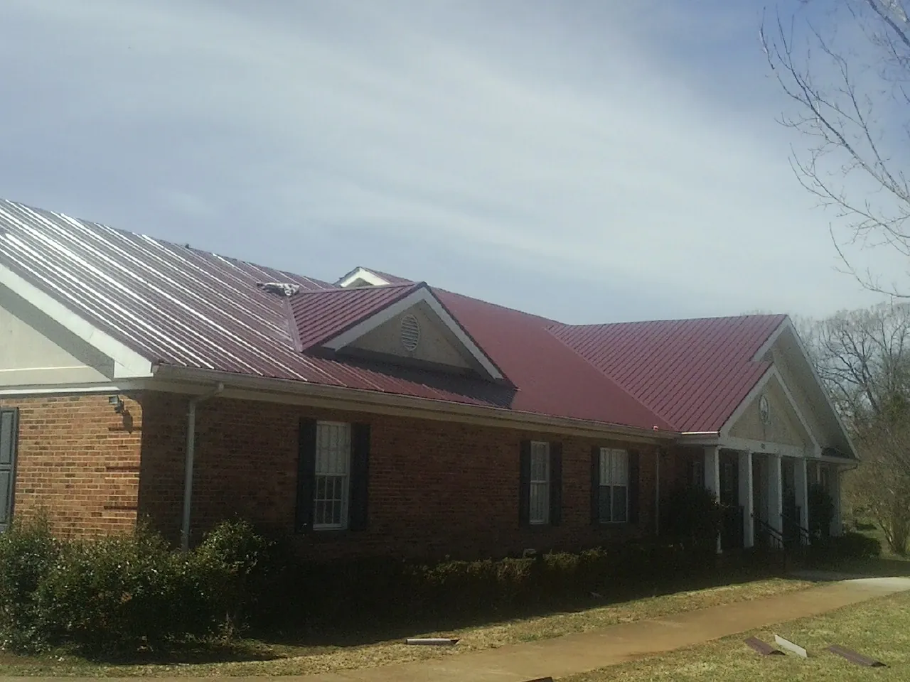 Red metal roof with gabled entries on a long brick building, from a Hail Damage Roof Repair job in Taylors Falls