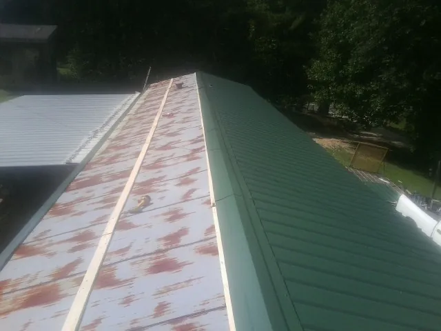Old rusted panels beside newly installed green metal roofing — Wind Damage Roof Repair by Roofing Brothers in Taylors Falls
