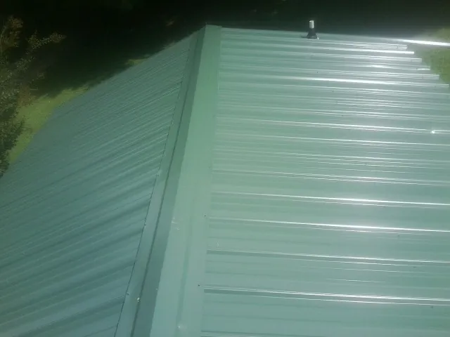 New green metal panels meeting at the ridge of a roof — Flat Roof Repair work by our crew in Taylors Falls