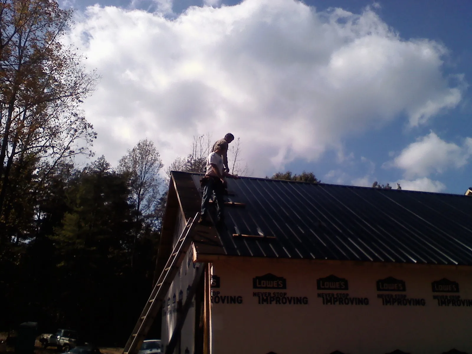 Roofer fastening dark metal panels high against a cloudy sky, from a Roof Inspection job in Taylors Falls