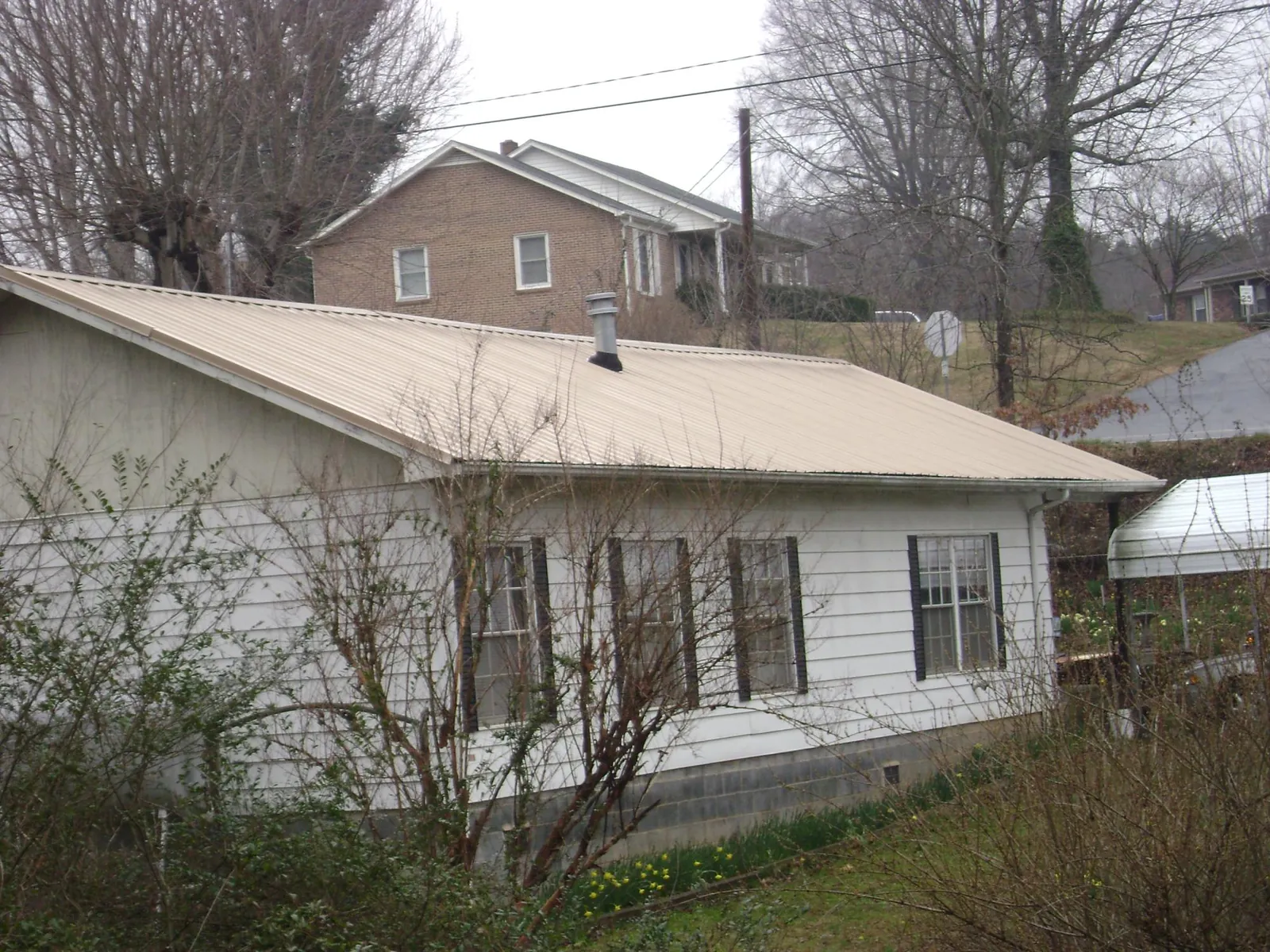 Tan metal roof on a white sided house set into a hillside — Commercial Roofing by Roofing Brothers in Taylors Falls