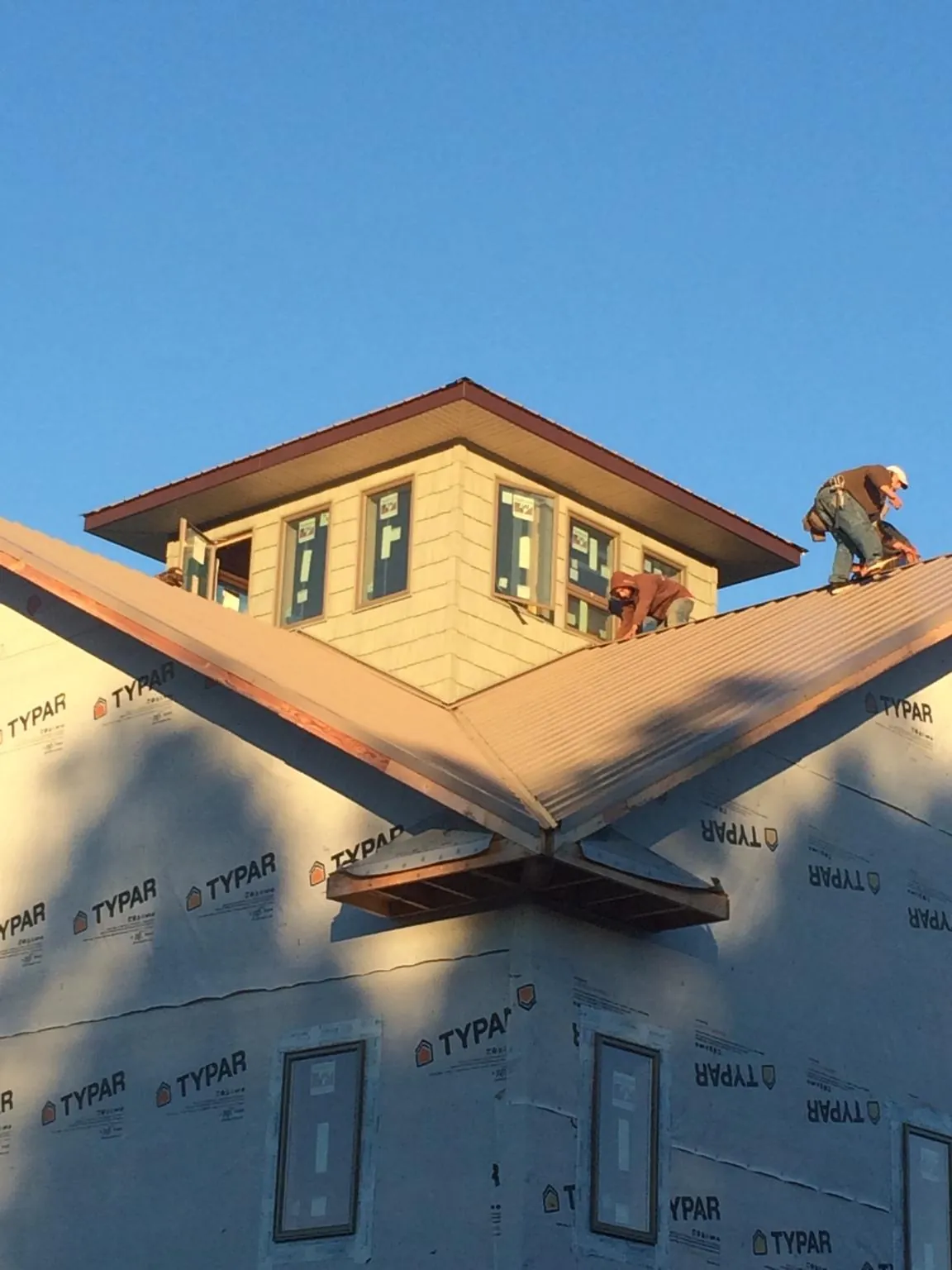 Roofers working around a rooftop cupola on a new metal roof at sunset in Taylors Falls